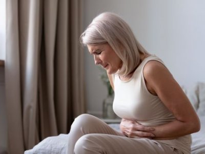 A woman in pain sitting on her bed clutching her stomach. 